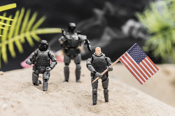 Selective focus of toy soldiers with guns holding american flag on sand dune — Stock Photo
