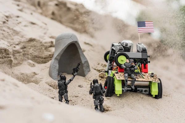 Soldados de brinquedo de plástico na duna de areia perto do carro com bandeira americana e caverna — Fotografia de Stock