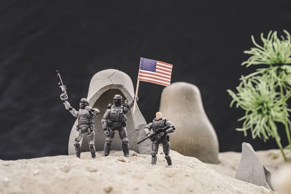 Selective focus of toy soldiers with guns and american flag standing near caves on sand dune — Stock Photo