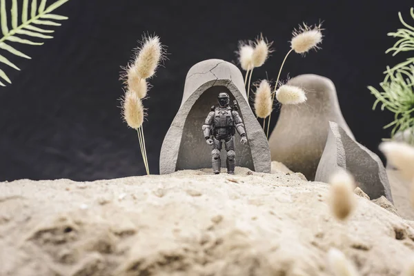 Selective focus of toy soldier with gun standing near caves on sand dune on black background — Stock Photo