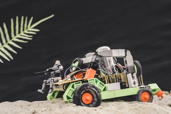 Игрушечный солдат с пистолетом сидит на машине на песчаной дюне на черном фоне — стоковое фото