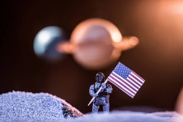Selective focus of toy astronaut holding american flag in space — Stock Photo