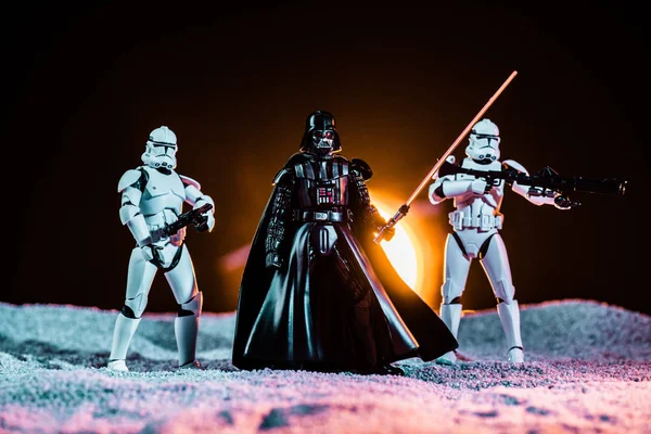 White imperial stormtroopers with guns and  Darth Vader with lightsaber on black background with sun — Photo de stock