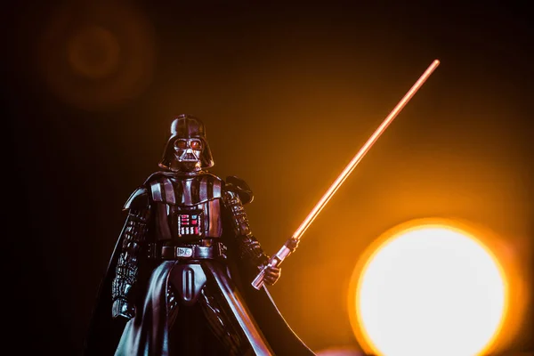 Darth Vader figurine with lightsaber on black background with shining sun — стокове фото