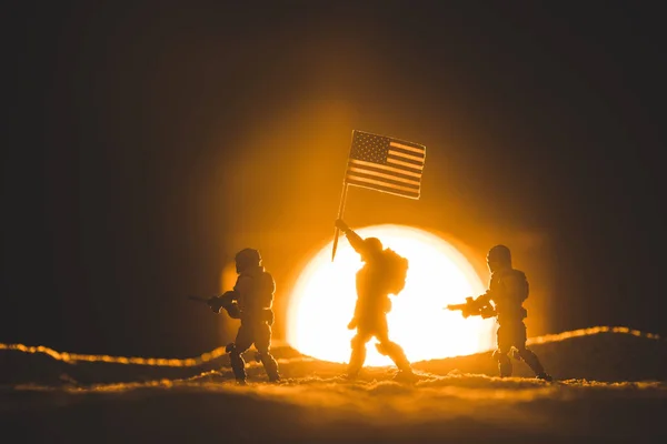 Selektiver Fokus von Spielzeugsoldaten-Silhouetten mit Gewehren und amerikanischer Flagge, die auf einem Planeten mit Sonne im Hintergrund wandeln — Stockfoto