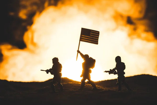 Juguete soldados siluetas con armas de fuego y bandera americana caminando en el planeta con el sol en el humo en el fondo - foto de stock