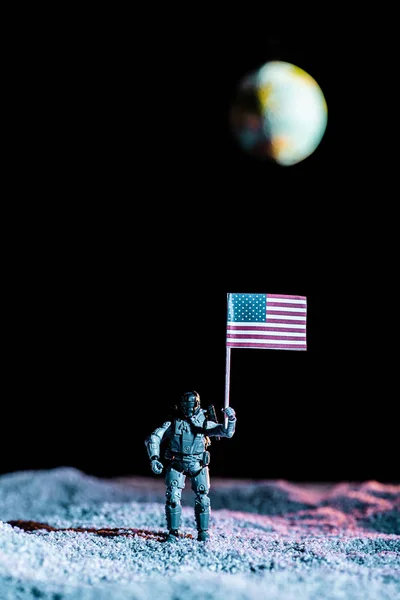Toy soldier holding national american flag in space with planet Earth on black background — Stock Photo
