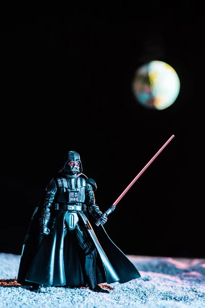 Darth Vader figurine with lightsaber on black background with planet Earth — Stock Photo