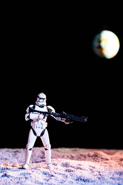 White imperial stormtrooper with gun on black background with blurred planet Earth — Fotografia de Stock