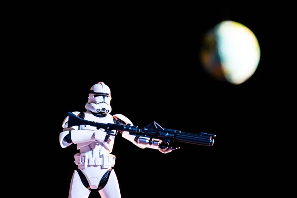 White imperial stormtrooper figure with gun on black background with blurred planet Earth - foto de stock