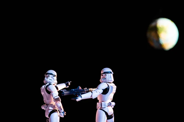 Selective focus of white imperial stormtroopers with weapon and planet earth isolated on black — стоковое фото