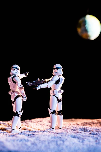 White imperial stormtrooper aiming with gun at another on black background with planet Earth — Stock Photo