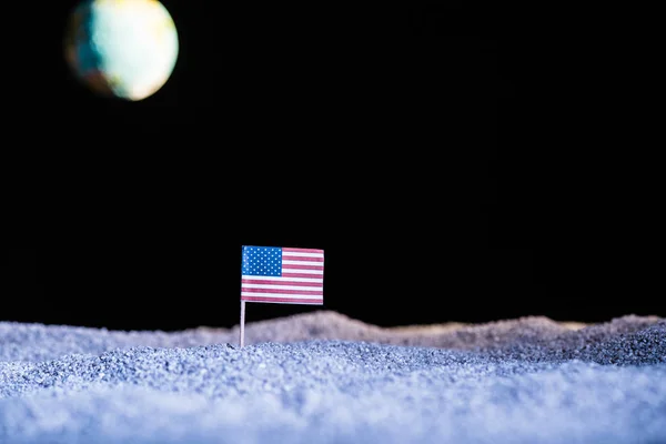 Sandy ground with american flag and blurred planet Earth in space isolated on black — Stock Photo