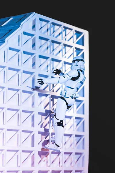 White plastic Imperial Stormtrooper climbing white textured wall isolated on black - foto de stock