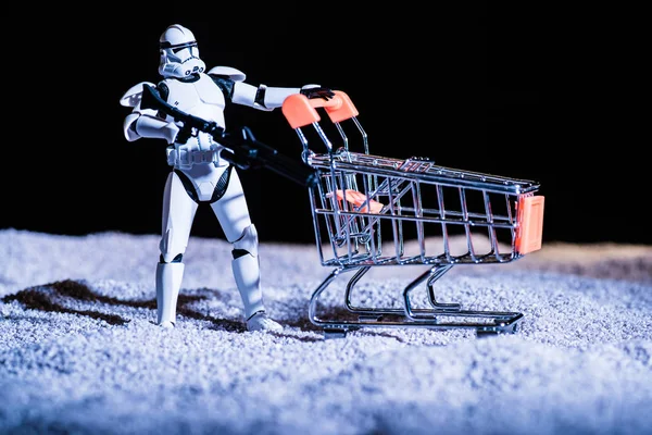 White plastic Imperial Stormtrooper with gun and shopping cart in space isolated on black — стокове фото