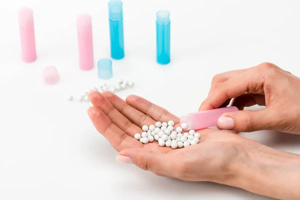 Cropped view of woman holding round pills in hand near blue and pink bottles on white — Stock Photo