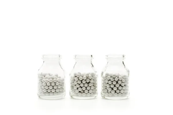 Bouteilles en verre avec de petites pilules rondes isolées sur blanc — Photo de stock