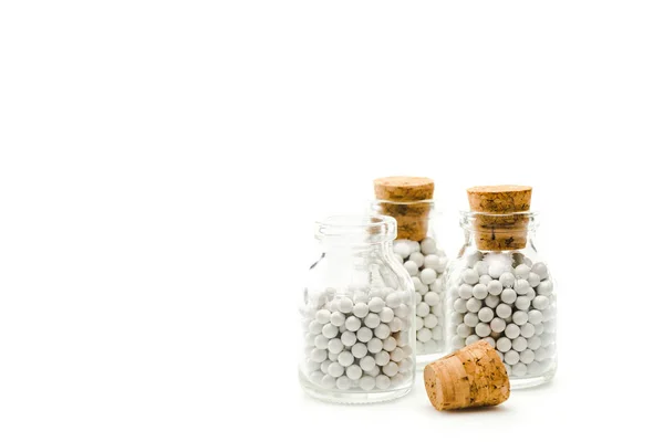 Bouteilles en verre avec de petites pilules rondes et bouchons en bois isolés sur blanc — Photo de stock