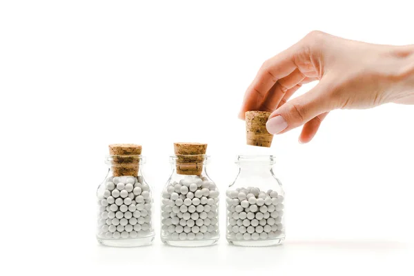 Vista recortada de la mujer tocando corcho de madera cerca de botellas de vidrio con pastillas aisladas en blanco - foto de stock