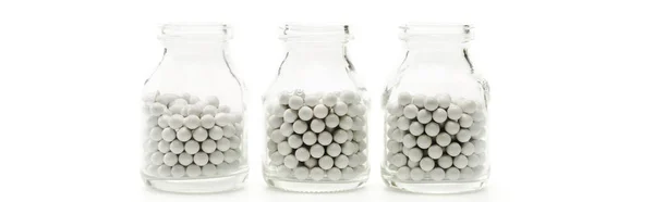 Plano panorámico de botellas de vidrio con pequeñas píldoras redondas aisladas en blanco - foto de stock