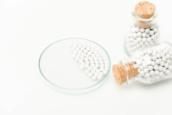 Foyer sélectif de petites pilules rondes dans une boîte de Pétri en verre près de bouteilles avec des bouchons en bois isolés sur blanc — Photo de stock