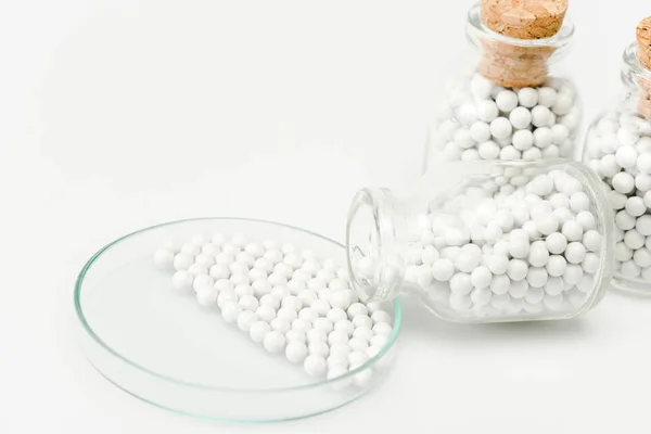 Enfoque selectivo de pequeñas píldoras en placa de Petri de vidrio cerca de botellas con corchos de madera aislados en blanco - foto de stock