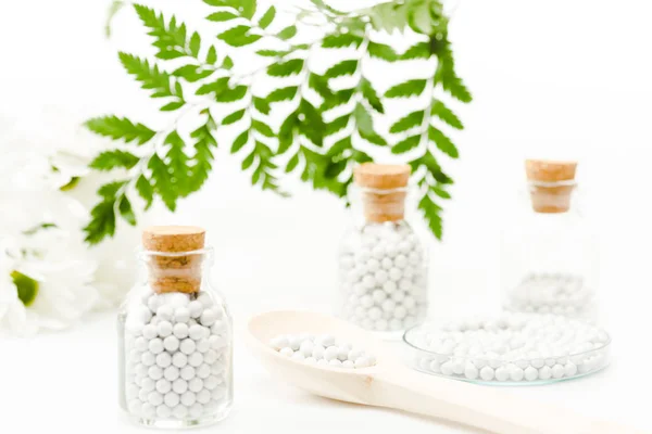 Selective focus of pills in glass bottles with wooden corks near green leaves on white — Stock Photo