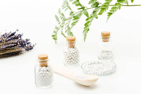 Selektiver Fokus der Medizin in Glasflaschen mit Holzkorken in der Nähe grüner Blätter auf weißem Grund — Stockfoto