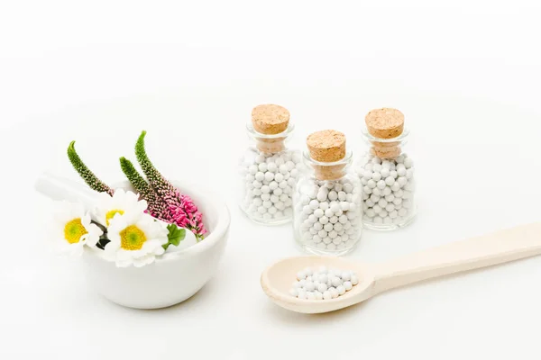 Fleurs en mortier près de pilon et bouteilles en verre avec des pilules sur blanc — Photo de stock