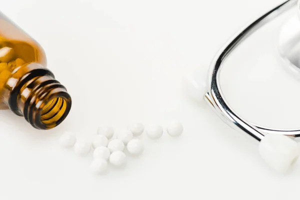 Foco seletivo de pequenas pílulas redondas perto de estetoscópio e garrafa de vidro no branco — Fotografia de Stock