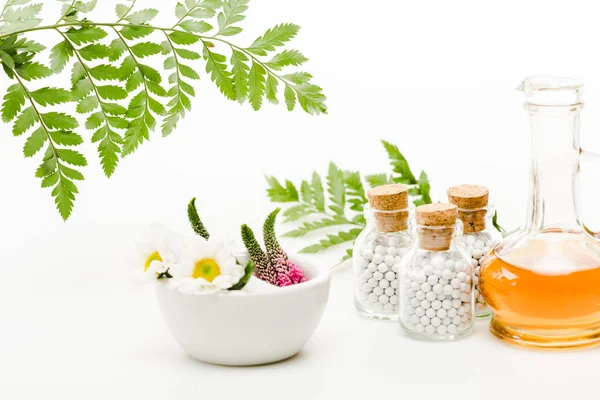 Fleurs en mortier près de pilon et bouteilles en verre avec des pilules, cruche à l'huile et feuilles vertes sur blanc — Photo de stock