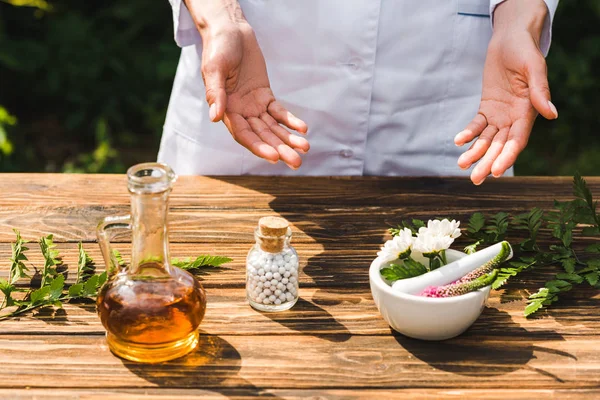 Abgeschnittene Ansicht einer Frau in der Nähe von Holztisch mit Pflanzen und Flasche mit Pillen — Stockfoto