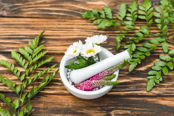 Top view of veronica and chrysanthemum flowers in mortar near pestle on wooden table — Stock Photo