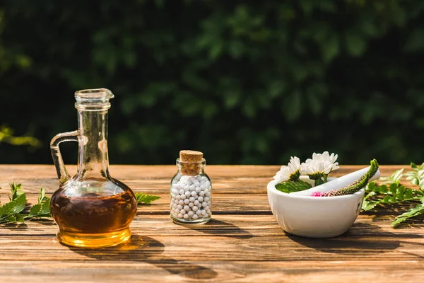 Botella de vidrio con pastillas cerca de flores en mortero cerca de pestle en la mesa de madera - foto de stock