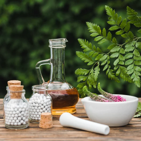 Selective focus of pestle near mortar with flowers, glass bottles and jug with oil on wooden table — Stock Photo