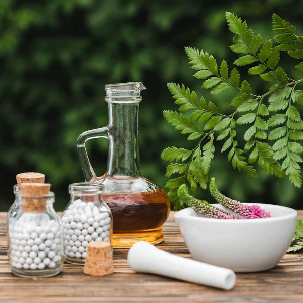 Messa a fuoco selettiva di pestello vicino malta con fiori, bottiglie di vetro e brocca con olio su tavolo di legno — Foto stock