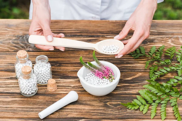 Draufsicht einer Frau, die einen Löffel mit Pillen in der Nähe eines Mörsers mit Veronika-Blüten und grünen Blättern auf einem Holztisch hält — Stockfoto