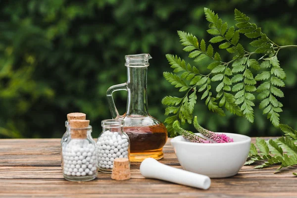 Selective focus of pestle near mortar with flowers, glass bottles with pills and jug with oil on wooden table — Stock Photo