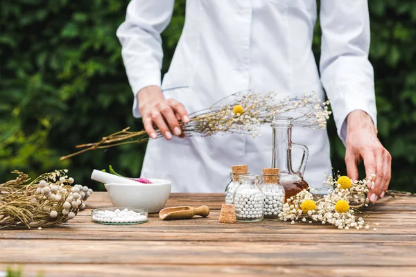 Cropped view of woman holding gypsophila flowers near bottles with pills — Stock Photo