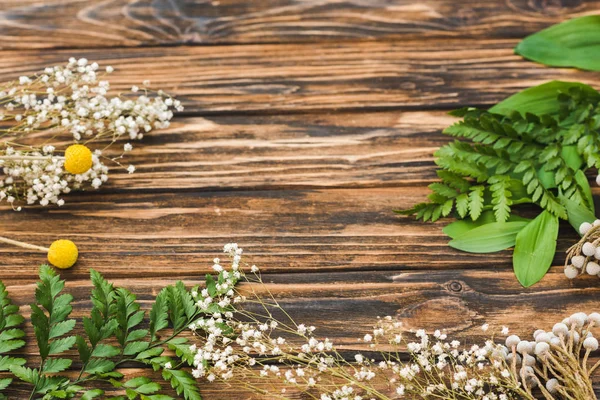 Draufsicht auf weiße und gelbe Blüten und grüne Blätter auf Holztisch — Stockfoto