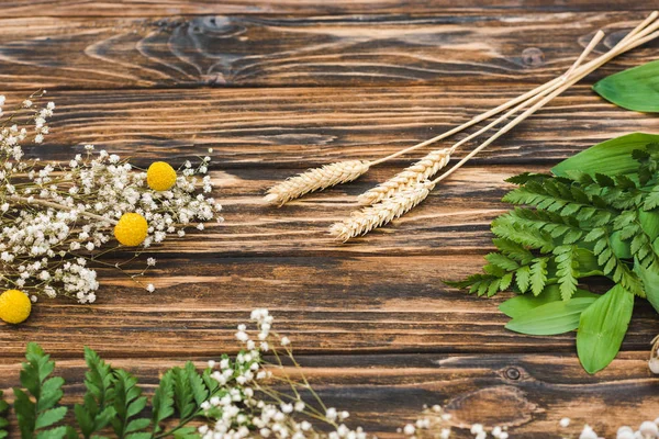 Vue de dessus des fleurs blanches et jaunes près des feuilles vertes sur la table en bois — Photo de stock