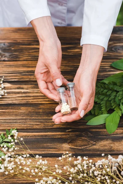 Cropped view of woman holding glass bottles with pills near green leaves — Stock Photo