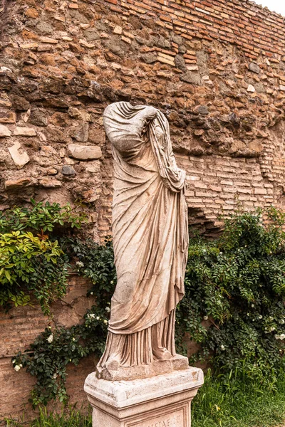 РИМ, ИТАЛИЯ - 28 ИЮНЯ 2019 г.: древняя безголовая статуя возле кирпичной стены и зеленых растений — стоковое фото
