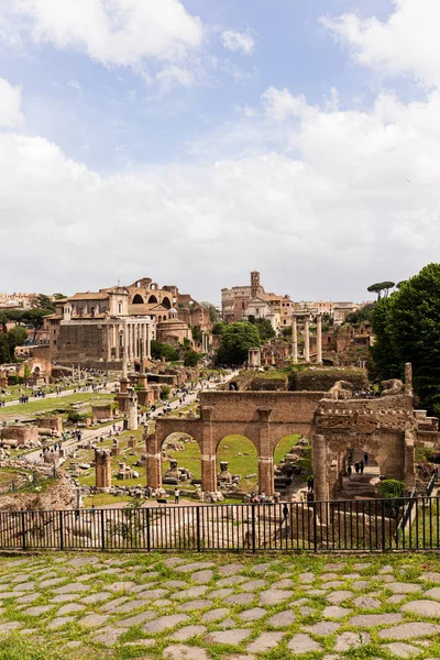 ROMA, ITÁLIA - 28 DE JUNHO DE 2019: turistas perto de edifícios antigos no fórum romano sob o céu azul — Fotografia de Stock