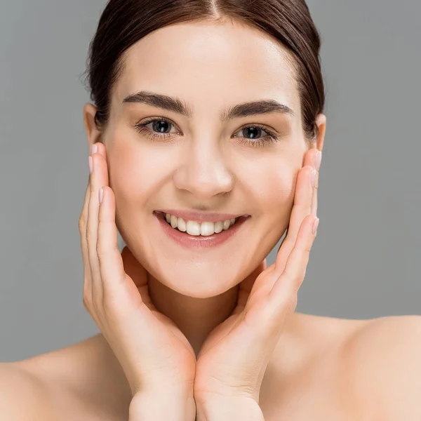 Close up of happy young naked woman looking at camera and touching face isolated on grey — Stock Photo