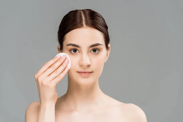 Attractive naked woman cleaning face with cotton pad isolated on grey — Stock Photo