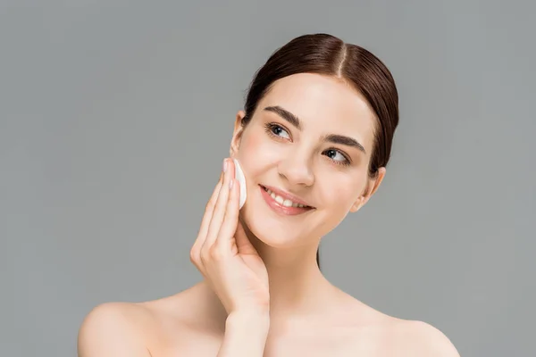 Happy naked woman cleaning face with cotton pad and smiling isolated on grey — Stock Photo