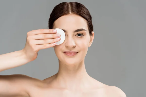 Cheerful naked woman covering eye with cotton pad isolated on grey — Stock Photo