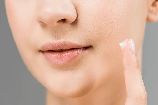 Cropped view of woman with cosmetic cream in finger isolated on grey — Stock Photo