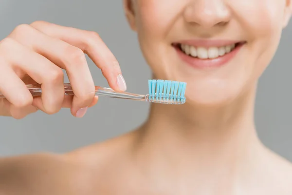 Обрезанный вид счастливой обнаженной женщины, держащей зубную щетку рядом с зубами, изолированными на сером — стоковое фото